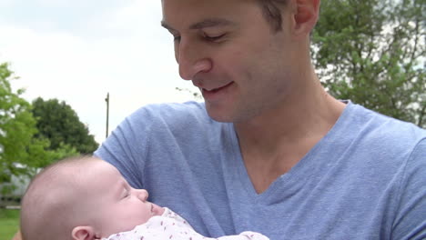 Slow-Motion-Shot-Of-Father-Cuddling-Baby-Daughter-In-Garden