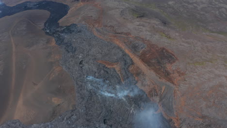 Spectacular-aerial-drone-view-of-vast-black-lava-river-in-Fagradalsfjall,-Iceland,-tilt-down-to-birds-eye-overhead-top-down-view,-day