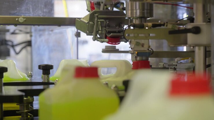 Automated capping head applies red caps to plastic chemical canisters moving on factory conveyor line