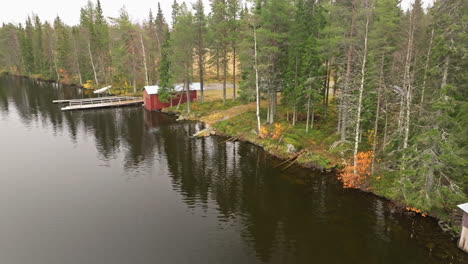 autumn forest and red fishermen houses at the calm lakeshore during cloudy morning in sweden