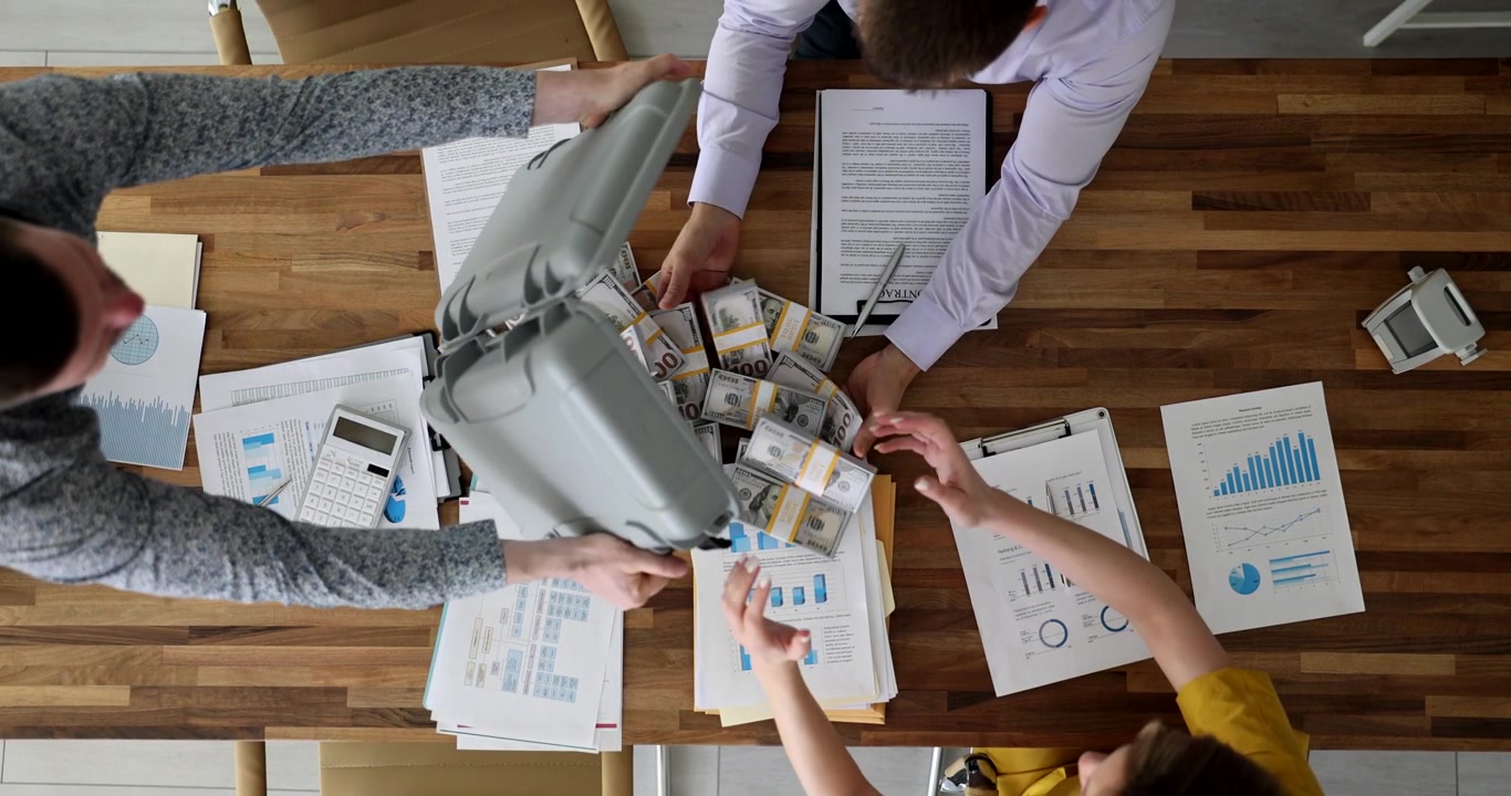 Colleague dumps pile of dollar bills onto table during meeting