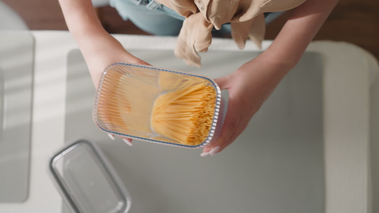 la señora examina el movimiento del recipiente de sacudida de espagueti crudo