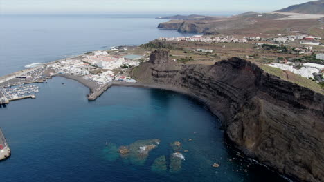 Panoramic-aerial-shot-over-the-port-of-Agaete,-appreciating-the-boats-at-the-dock-and-the-houses