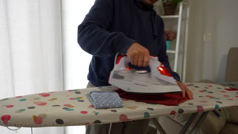 man ironing baby clothes at home, doing chores with care and focus indoors