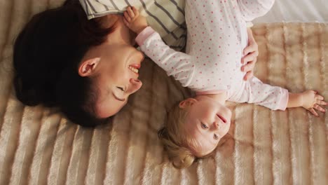 overhead view of caucasian mother and baby playing together while lying on the bed at home