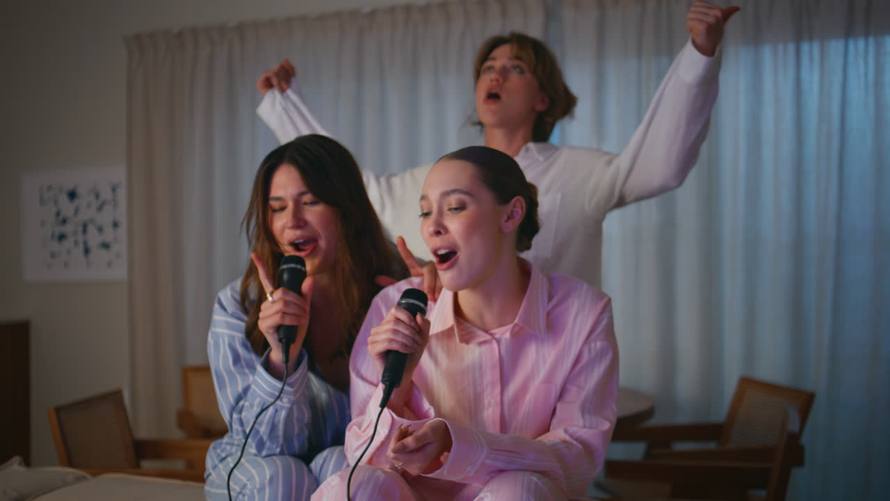 Happy women singing karaoke in pajamas at friendly sleepover. Girls having fun