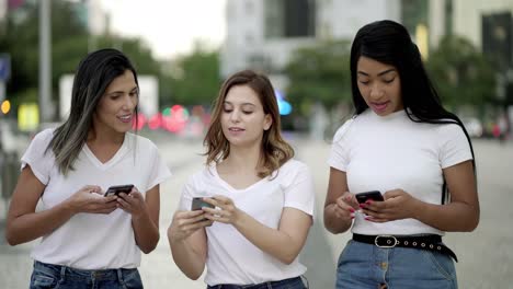 Amigos-Alegres-Caminando-Por-La-Calle-Y-Enviando-Mensajes-De-Texto-En-Teléfonos-Inteligentes