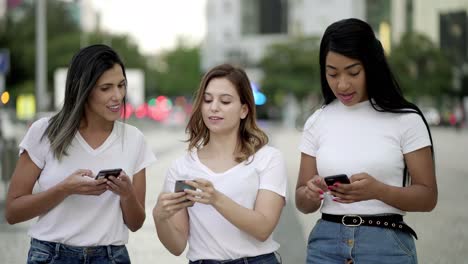 amigos alegres caminando por la calle y enviando mensajes de texto en teléfonos inteligentes