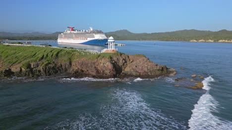 Aerial-view-of-large-Cruiser-docking-in-terminal-of-Puerto-Plata-during-sunny-day---In-foreground-beautiful-hill-with-pavilion-of-Senator-Resort-,Dominican-Republic