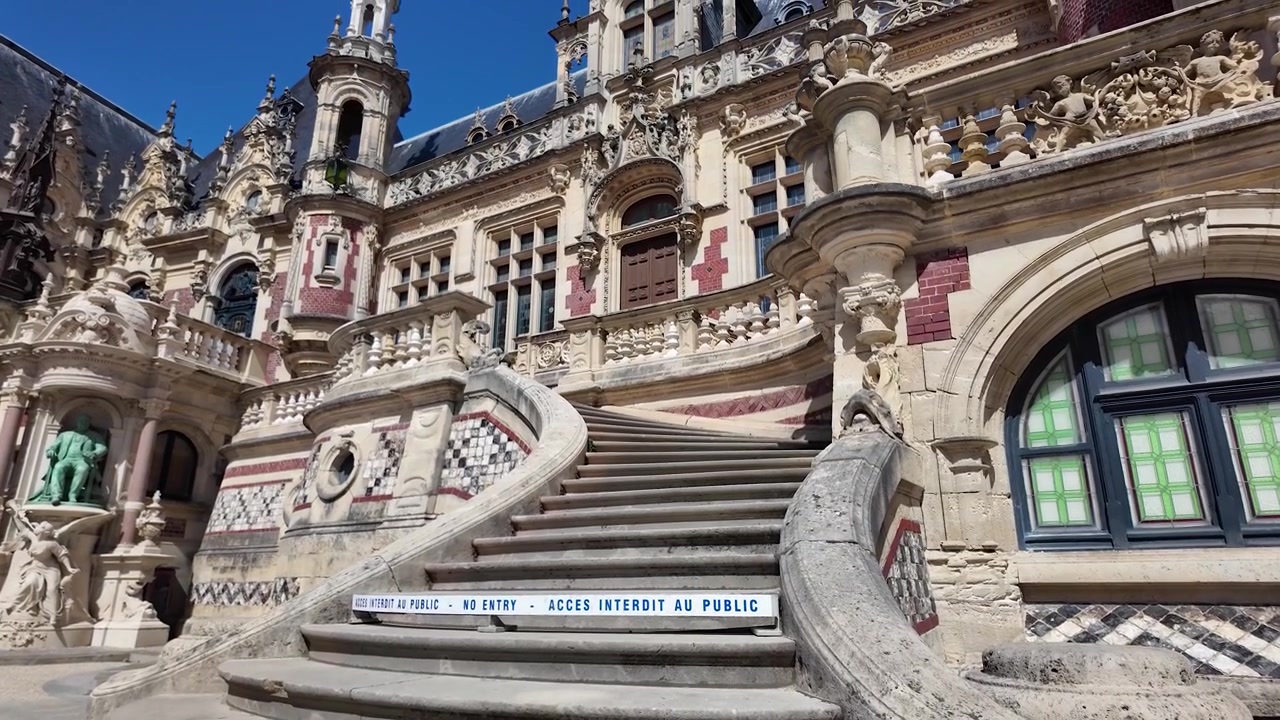 Movimento lento de aproximação em direção à escadaria principal do Palais Bénédictine em Fécamp, exibindo sua fachada ornamentada, trabalhos em pedra esculpida, estátuas e balaustradas decorativas