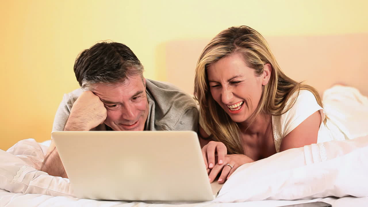 una pareja sonriente mirando una computadora portátil en la cama