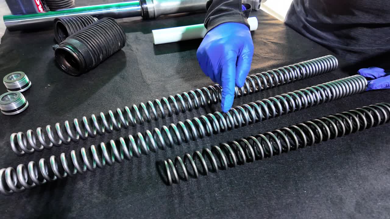 Close-up professional technician's gloved hand pointing at different helical coil springs to determine the optimal spring rate for performance tuning
