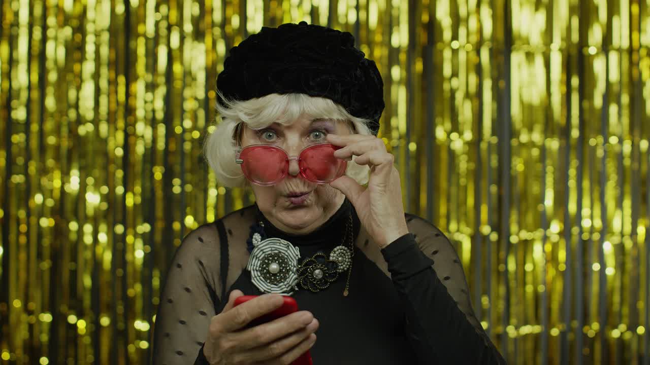 충격을 받은 노인 여성이 소셜 네트워크에서 메시지를 입력하고, 앱을 사용하고, 온라인 쇼핑을 하고, 느린 동작을 하고 있습니다.