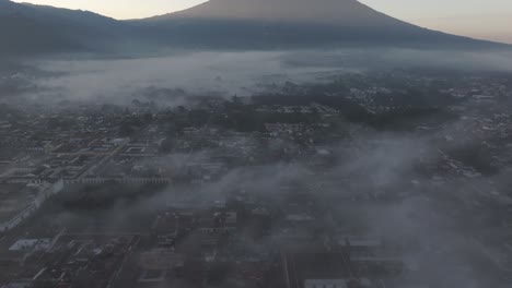 Volando-Hacia-Atrás-En-La-Ciudad-De-Antigua-Guatemala-Durante-La-Mañana-Brumosa,-Aérea