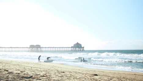 A-family-goes-surfing-at-the-beach-during-a-hazy-sunrise-with-the-Huntington-Beach-Pier-in-the-background-at-Surf-City-USA-California