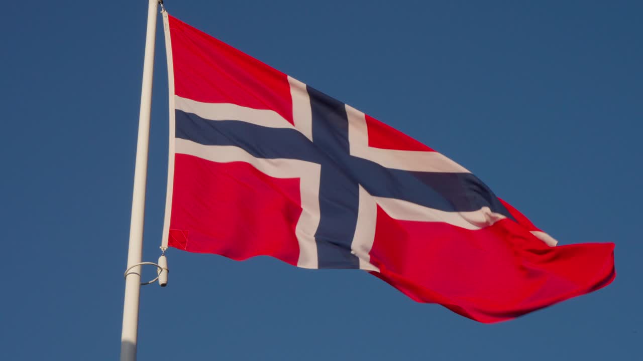 Close-up of Norway's flag with red background and blue cross fluttering in sunlight. Clear sky. Location: Oslo, Norway