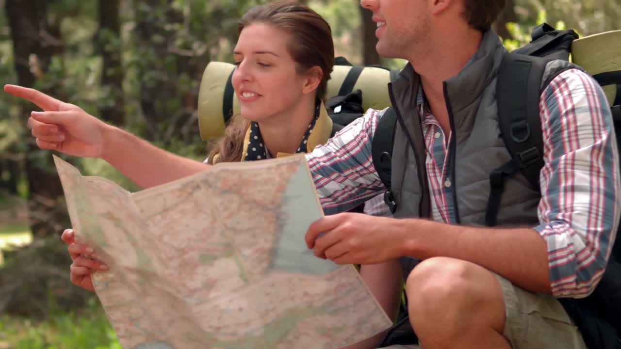 pareja sonriente con un mapa en una caminata en el campo