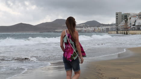 Filmaufnahme-Bei-Sonnenaufgang-Einer-Frau,-Die-Am-Strand-Von-Las-Canteras-Spazieren-Geht-Und-Die-Häuser-In-Der-Gegend-Sieht