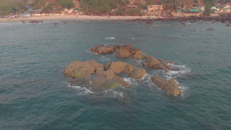 Rock-formation-lurking-above-the-sea-near-Arambol-Beach-at-dusk,-in-Goa,-India---Aerial-Low-angle-Orbit