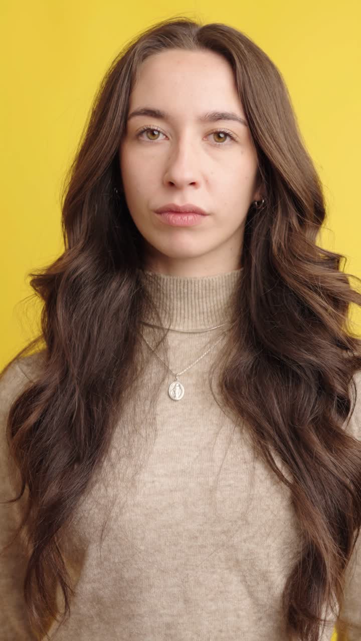 Young woman with long hair posing against yellow backdrop
