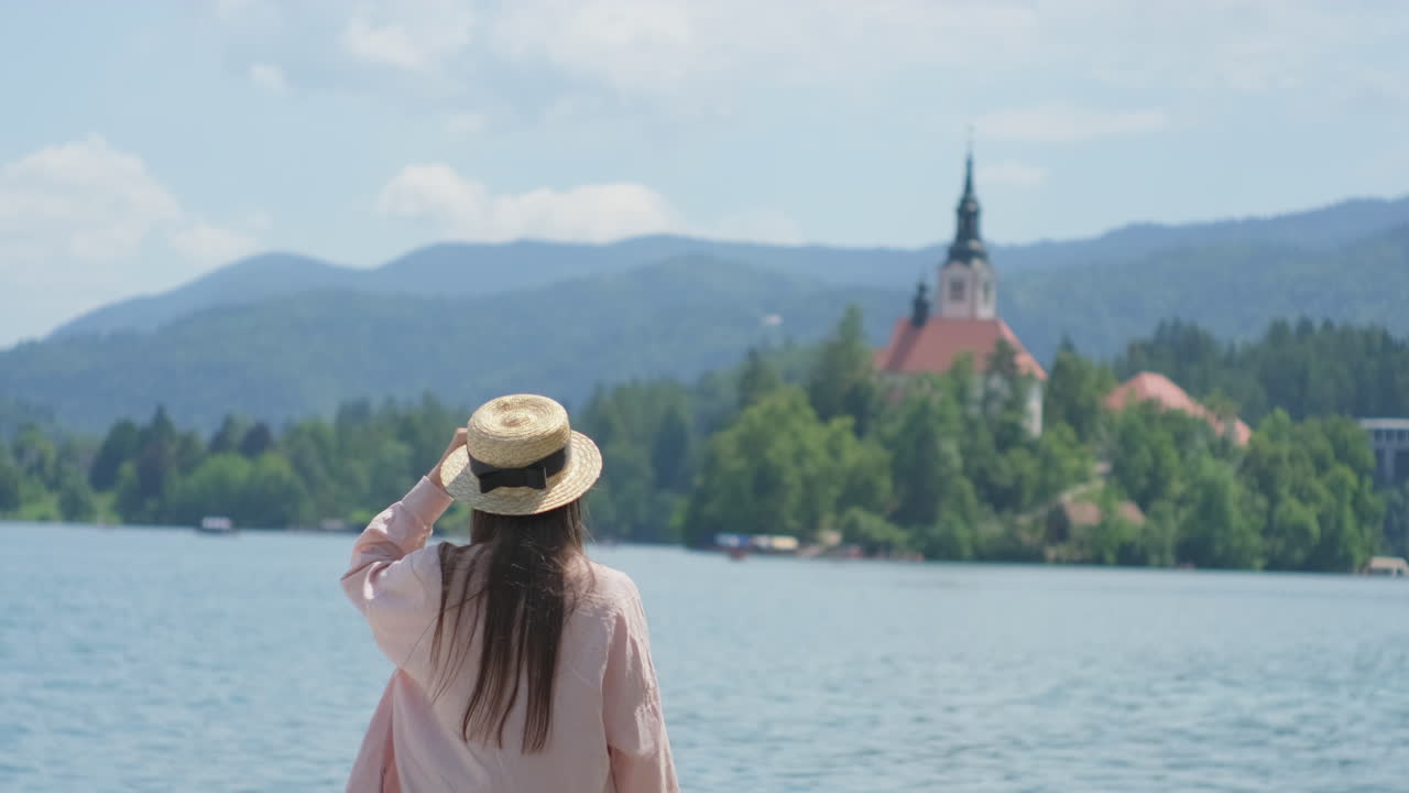 mujer disfrutando de la vista de un lago, montañas e iglesia