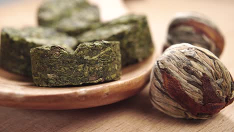 hojas de té verde secas trenzadas y prensadas en bolas y pastillas en una cuchara de madera sobre una mesa de madera