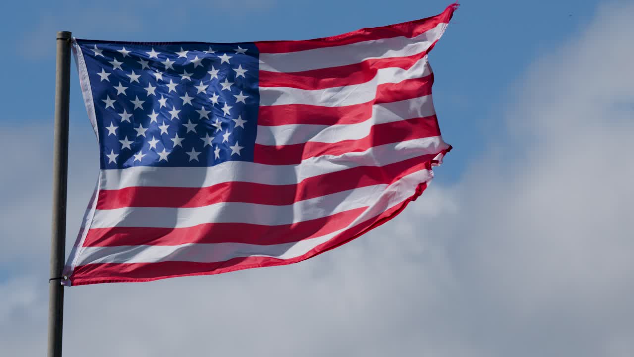 United States flag flutters dynamically on flagpole, daylight, clear sky, medium shot, natural lighting