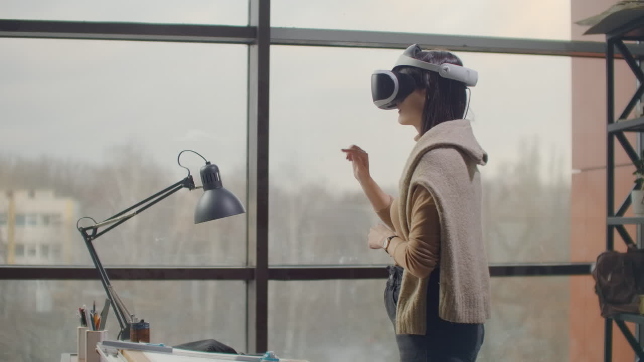 ingeniera femenina en un casco de realidad virtual cerca de la ventana grande con sus manos imita el trabajo de la interfaz. diseñando el futuro el concepto de arquitectura virtual y aplicaciones gráficas de interfaz de diseño.