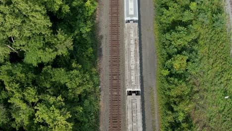 top down aerial and tilt reveals stopped train cars on track, rail travel, transport concept, drone view, green grass and trees in summer line the track