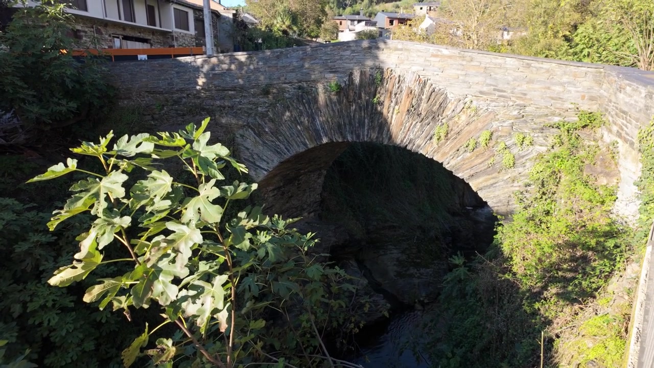 L'accesso al ponte in pietra presenta figure di pellegrini e fiori a Éntoma, Galizia, Spagna