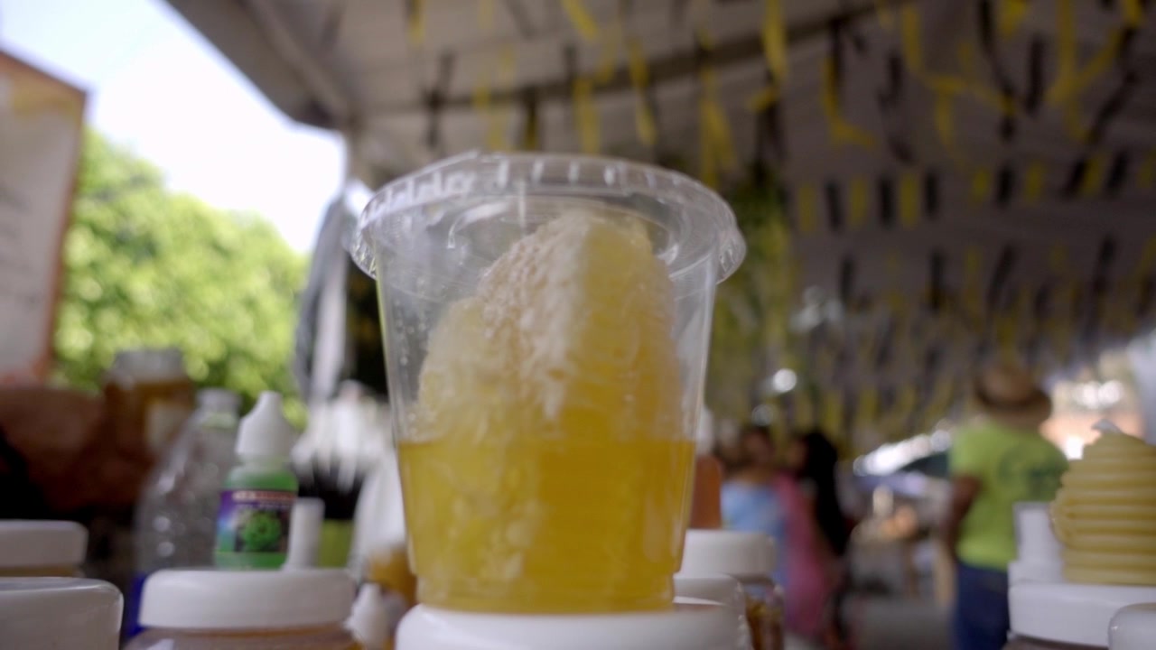 Close up of a honeycomb placed in a plastic cup filled with fresh honey featuring natural honeycomb texture golden color and sweet food displayed at a market.