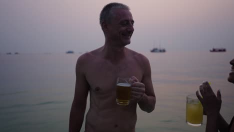 man and woman toasting with drinks in the ocean at sunset
