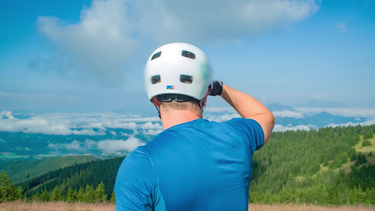 tiro circular en forma de ciclista masculino caucásico con casco, mirando la hermosa vista de las montañas y las nubes, tiro medio