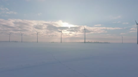 establecimiento de una vista aérea de las turbinas eólicas que generan energía renovable en el parque eólico, un paisaje rural lleno de nieve con niebla, un día soleado de invierno, un amplio tiro de drones que avanza bajo