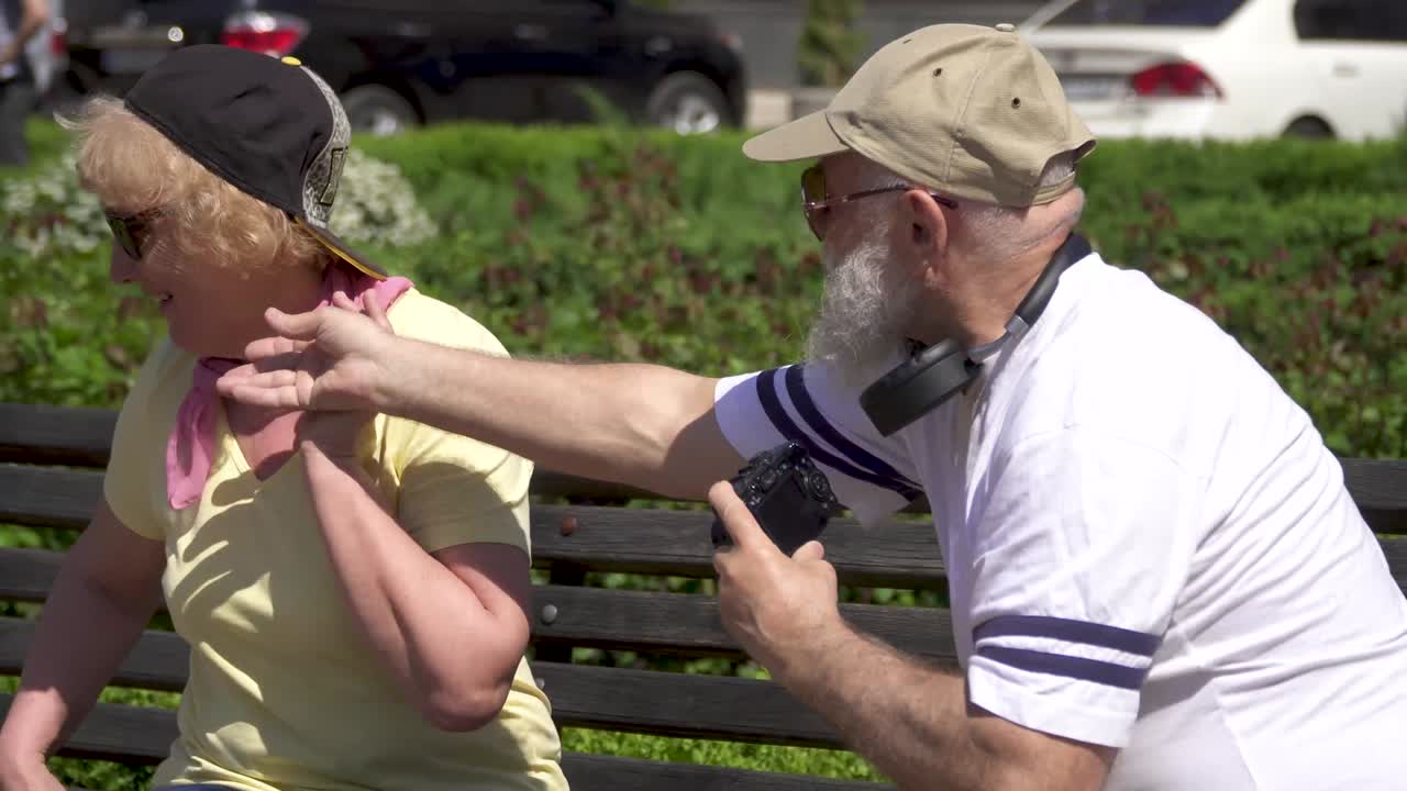 성숙한 남자가 공원의 벤치에서 그의 세련된 아름다운 아내를 사진으로 찍습니다.