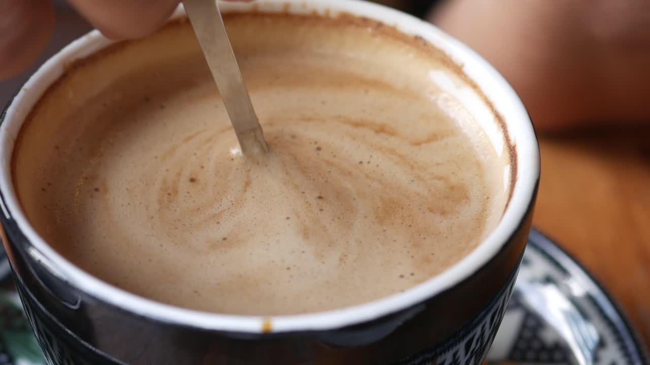 Close-up of a hand stirring a foamy coffee in a cup