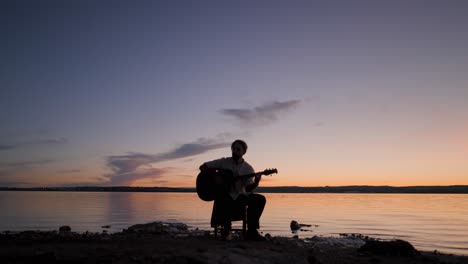 Man playing guitar at sunset by the lake