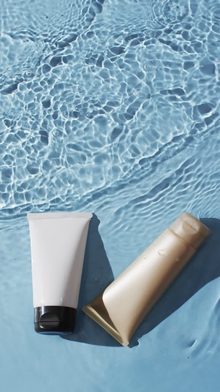 Vertical video of beauty product tubes in water with copy space on blue background