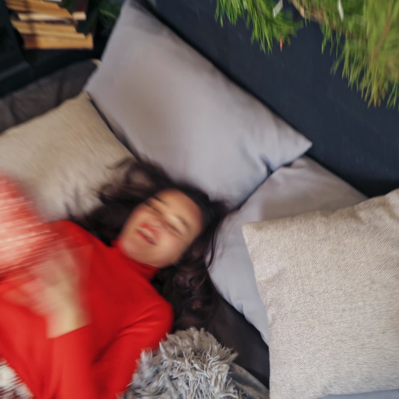 Attractive girl in red on bed with gifts. Cheerful young woman enjoying spare time while laying on bed in Christmas decorated bedroom. Top view.