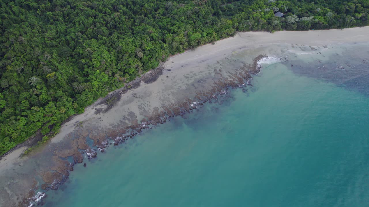 Ondas na praia respingando na costa de Cape Tribulation com floresta tropical densa no Norte Tropical de Queensland, Austrália.
