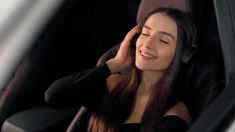 Retrato-De-Una-Joven-Hermosa-Sentada-En-El-Auto-Escuchando-Música-Con-Auriculares