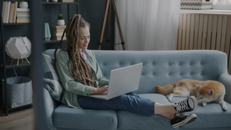 Woman working on laptop on a couch with a dog