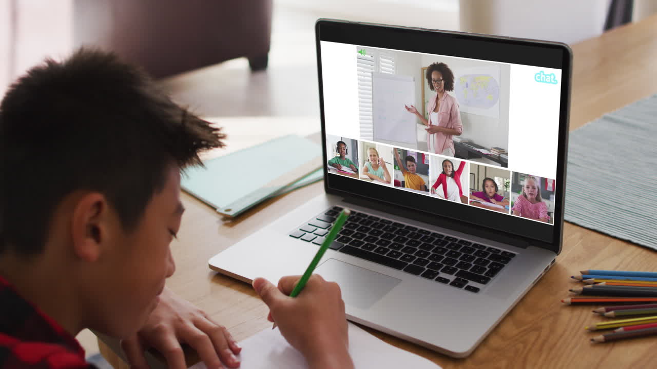 Schoolboy using laptop for online lesson at home, with diverse teacher and class on screen