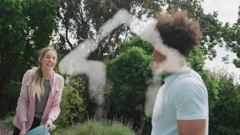 animation of cloud house over happy diverse couple having pillow fight in garden