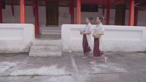 two girls in thai traditional dress walking near temple, slow motion