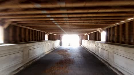 Aerial-fast-fly-into-the-historic-covered-wooden-bridge-over-the-creek-in-a-small-American-town