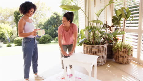 mother and adult daughter enjoying coffee and conversation on patio with plants nearby