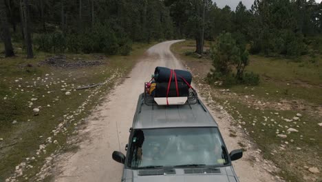 front side view of a jeep with roof racks driving on mountain road in forest, car trip to the mountain top, aerial