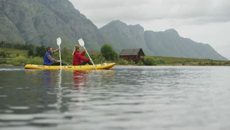 Pareja-Caucásica-Pasando-Un-Buen-Rato-En-Un-Viaje-A-Las-Montañas,-Haciendo-Kayak-Juntos-En-Un-Lago