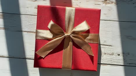 red gift box with gold ribbon on a white wooden background